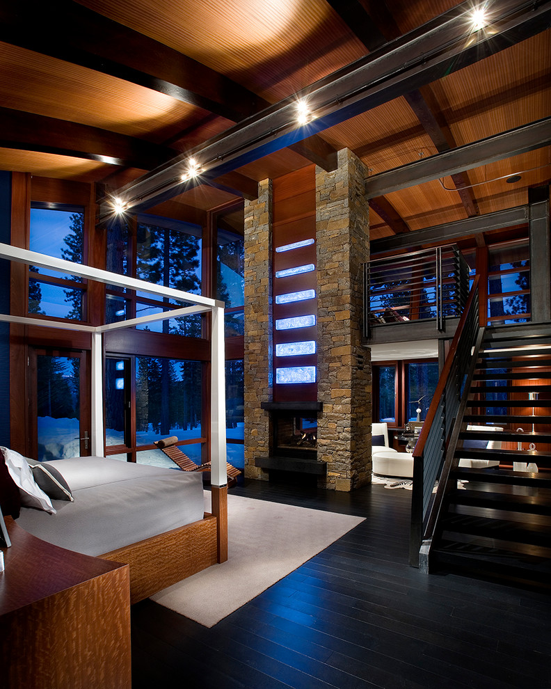 Стильный дизайн: большая хозяйская спальня в стиле модернизм с коричневыми стенами, деревянным полом, двусторонним камином, фасадом камина из камня и черным полом - последний тренд