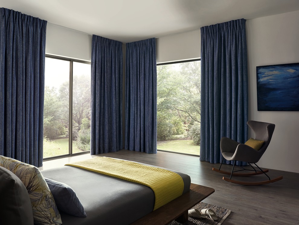 На фото: большая хозяйская спальня в стиле модернизм с белыми стенами, темным паркетным полом, коричневым полом и синими шторами с