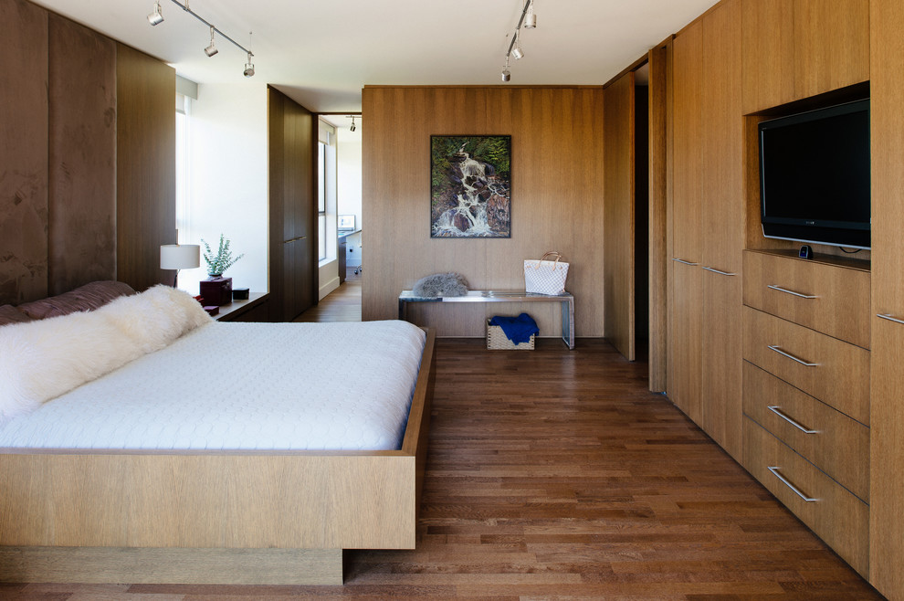 Idee per una camera da letto design con pavimento in legno massello medio e TV