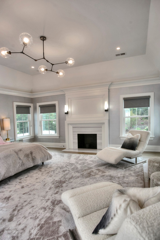 Großes Klassisches Hauptschlafzimmer mit grauer Wandfarbe, hellem Holzboden, Kamin, Kaminumrandung aus Stein und grauem Boden in New York