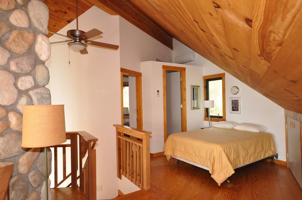 Modelo de dormitorio tipo loft rural pequeño con paredes blancas, suelo de madera clara, todas las chimeneas y marco de chimenea de piedra