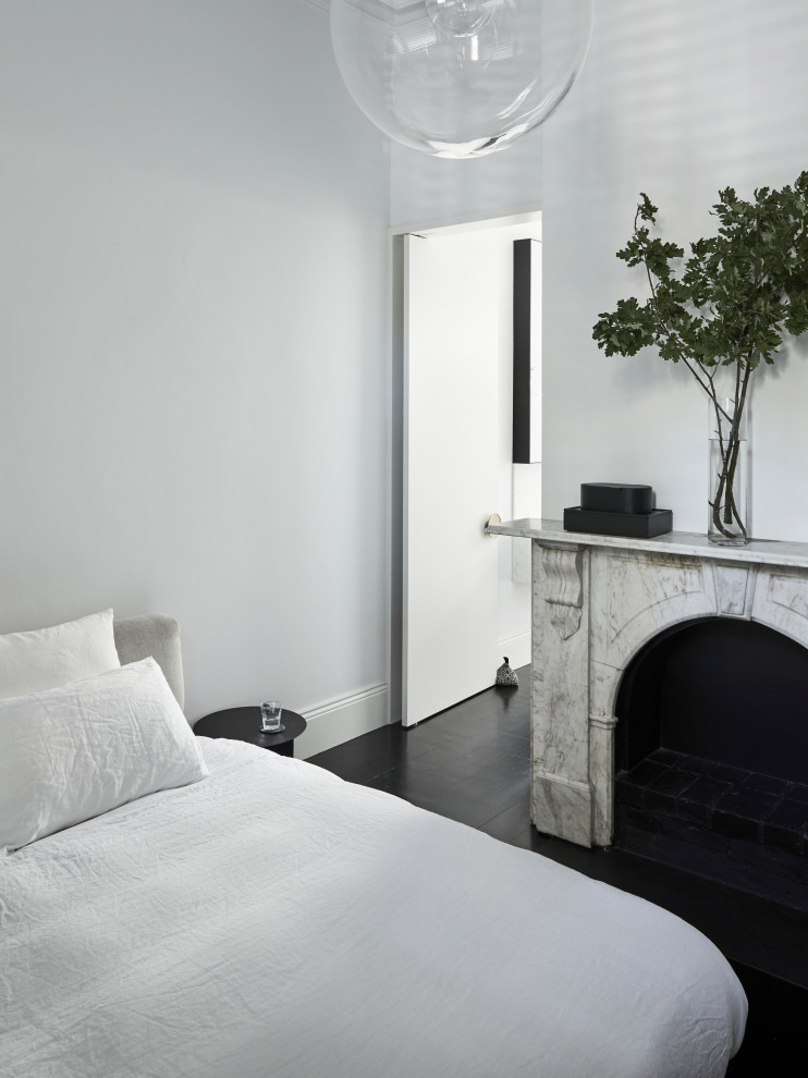 Источник вдохновения для домашнего уюта: спальня в современном стиле с белыми стенами, стандартным камином, фасадом камина из камня, черным полом и темным паркетным полом