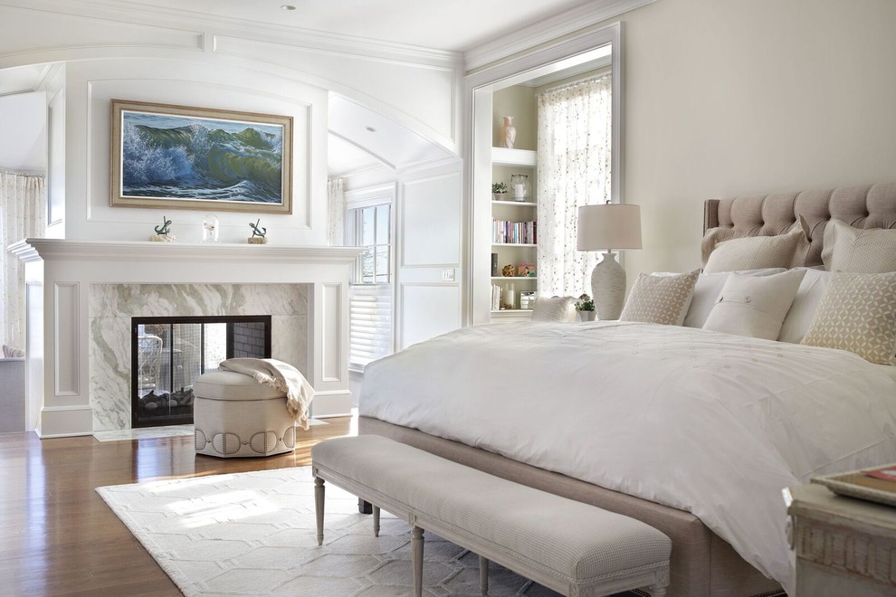 Klassisches Hauptschlafzimmer mit beiger Wandfarbe, dunklem Holzboden, Tunnelkamin, Kaminumrandung aus Stein und braunem Boden in New York