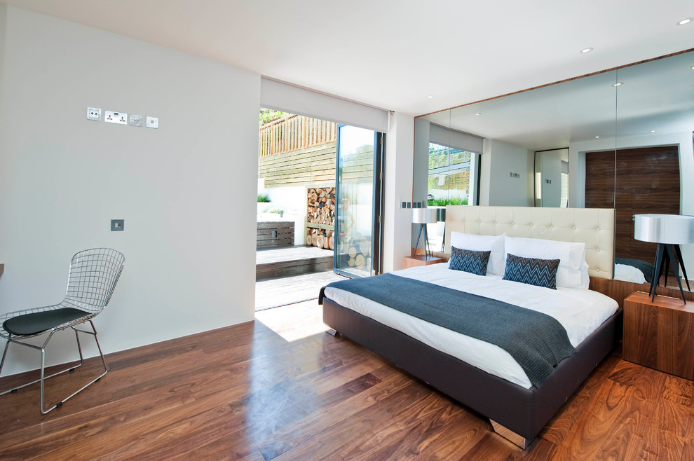 Foto på ett funkis sovrum, med vita väggar och mellanmörkt trägolv