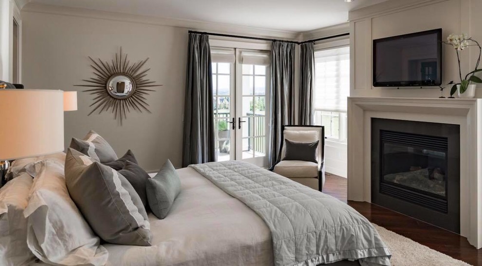 Klassisches Schlafzimmer mit beiger Wandfarbe, dunklem Holzboden, Kamin, Kaminumrandung aus Metall und braunem Boden in Calgary
