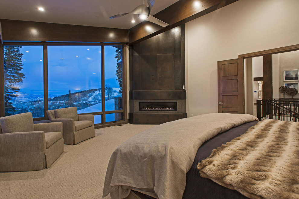 На фото: огромная хозяйская спальня в современном стиле с серыми стенами, ковровым покрытием, угловым камином, фасадом камина из металла, бежевым полом и балками на потолке