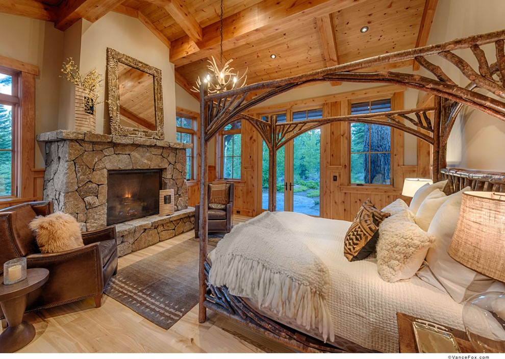 Imagen de dormitorio principal rural con paredes beige, suelo de madera clara, todas las chimeneas y marco de chimenea de piedra