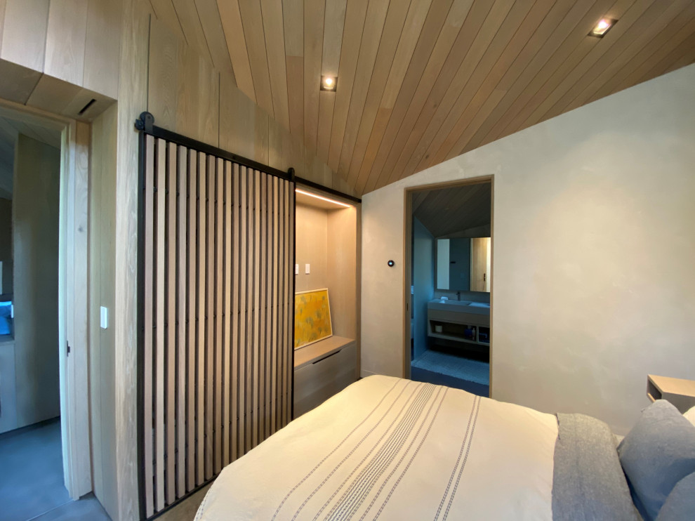 Immagine di una camera degli ospiti minimal di medie dimensioni con pareti beige, pavimento in cemento, pavimento grigio, soffitto in legno e pareti in legno