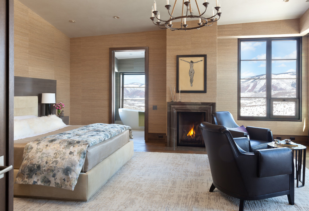 Ejemplo de dormitorio principal rústico con paredes beige, suelo de madera en tonos medios, todas las chimeneas y marco de chimenea de piedra