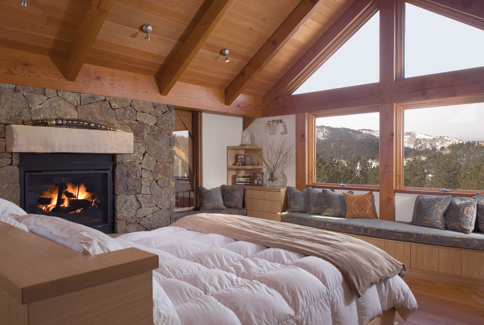Ejemplo de dormitorio principal rústico con paredes blancas, suelo de madera en tonos medios, todas las chimeneas, marco de chimenea de piedra y suelo marrón