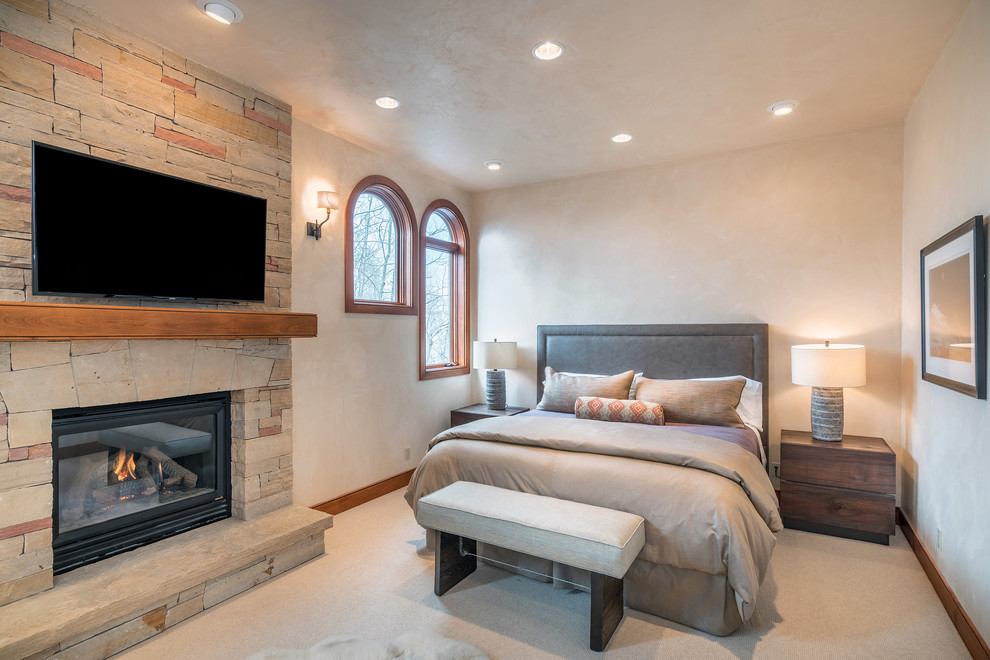 Design ideas for a large contemporary master bedroom in Denver with beige walls, a standard fireplace, a stone fireplace surround and carpet.