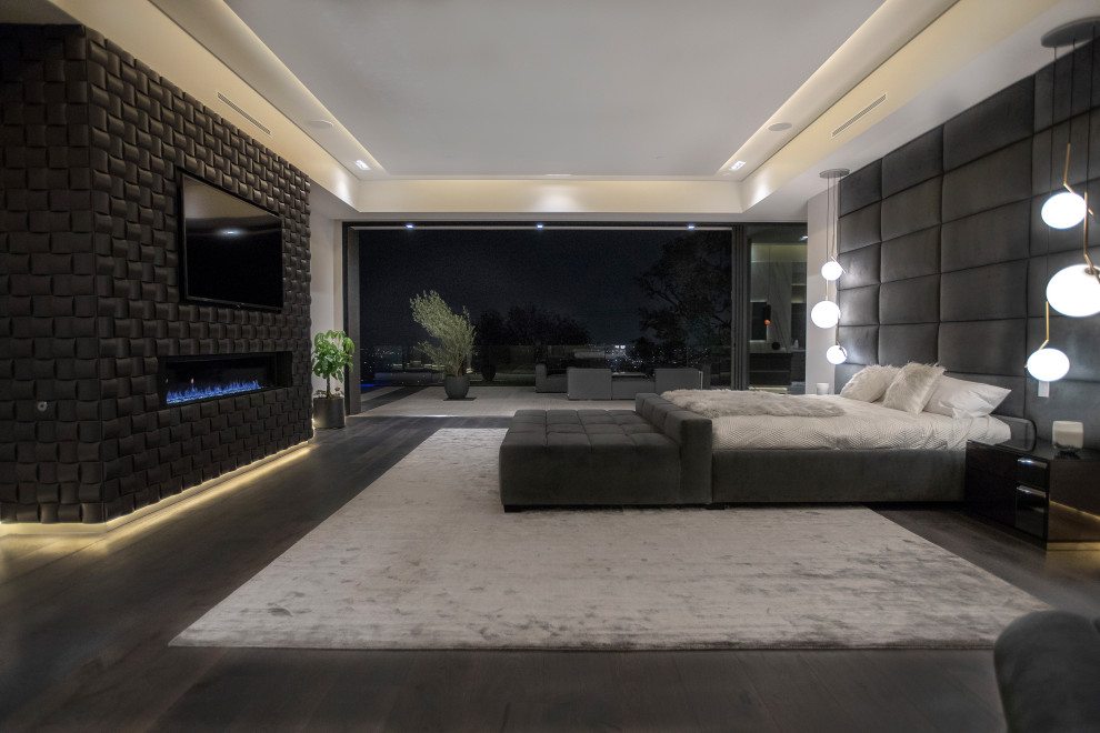 Ejemplo de dormitorio principal minimalista grande con paredes blancas, suelo de madera oscura, chimenea lineal, marco de chimenea de baldosas y/o azulejos y suelo marrón