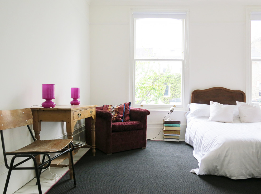 This is an example of an eclectic grey and pink bedroom in London with white walls and black floors.