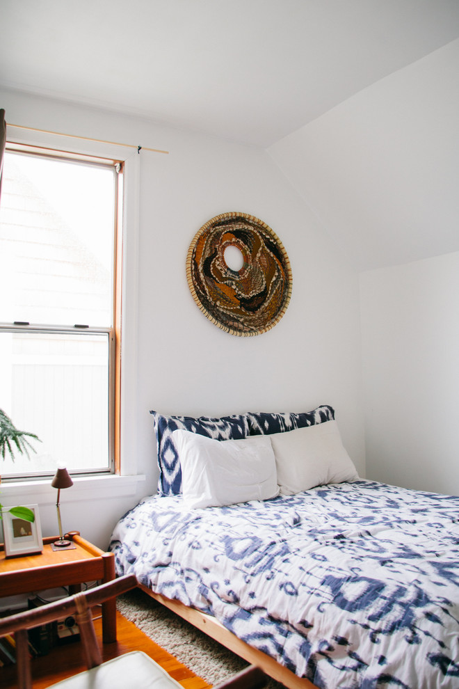 Réalisation d'une petite chambre d'amis bohème avec un mur blanc et un sol en bois brun.