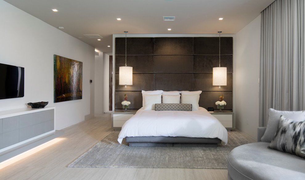 Expansive contemporary master bedroom in Orlando with white walls, light hardwood flooring, a standard fireplace and a stone fireplace surround.