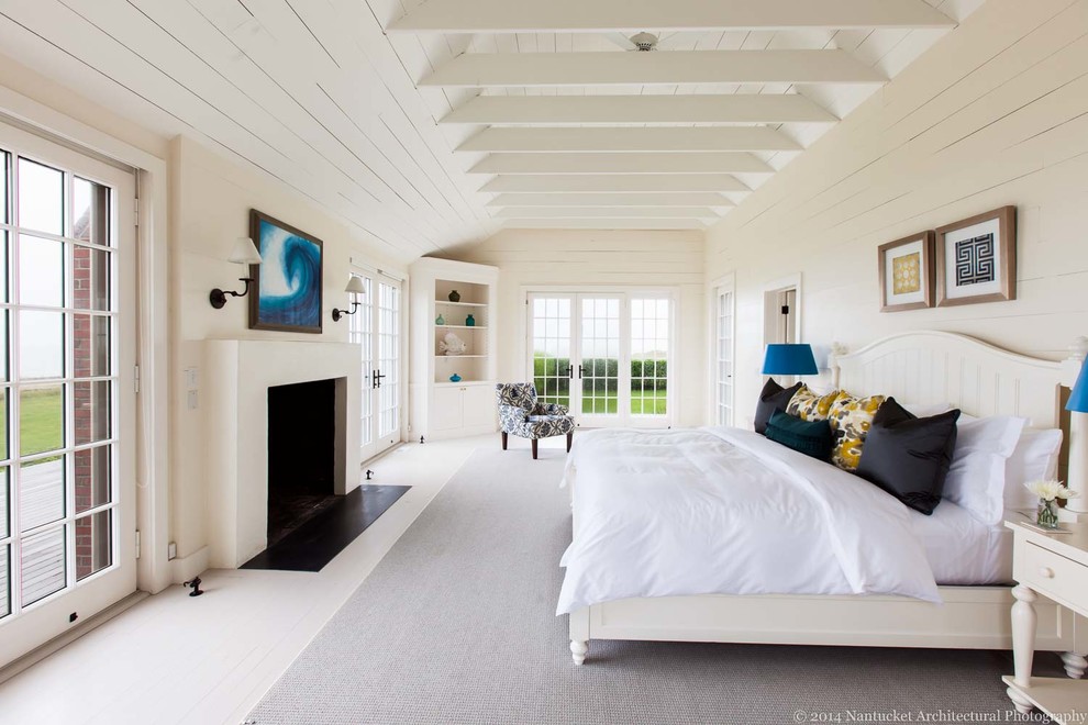 Ejemplo de dormitorio principal costero grande con paredes blancas, suelo de madera pintada, todas las chimeneas y marco de chimenea de yeso