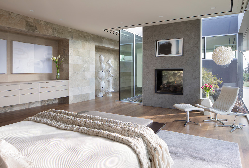 Aménagement d'une grande chambre parentale moderne avec un mur beige, une cheminée double-face, un manteau de cheminée en plâtre, parquet clair et un sol beige.