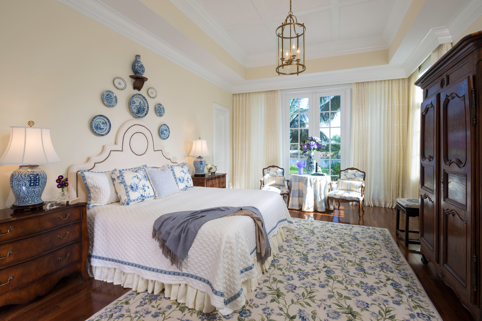 Photo of a large traditional master bedroom in Miami with yellow walls and dark hardwood flooring.