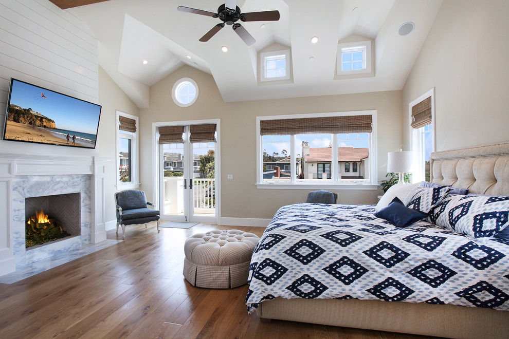 Maritimes Schlafzimmer mit beiger Wandfarbe, braunem Holzboden, Kamin und Kaminumrandung aus Stein in Orange County