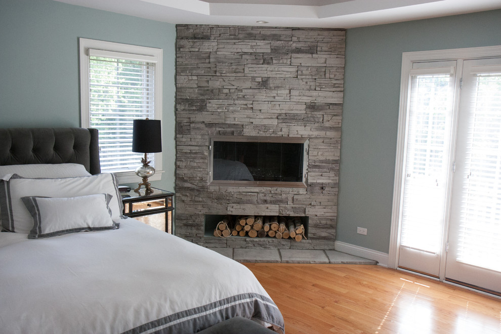 Kleines Modernes Hauptschlafzimmer mit blauer Wandfarbe, Kalkstein, Eckkamin, Kaminumrandung aus Stein und braunem Boden in Chicago