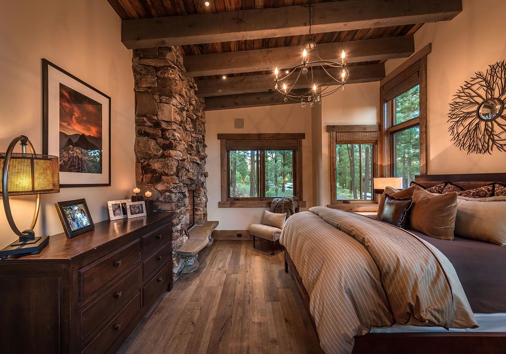 Ejemplo de dormitorio rústico con paredes marrones, suelo de madera oscura, todas las chimeneas y marco de chimenea de piedra