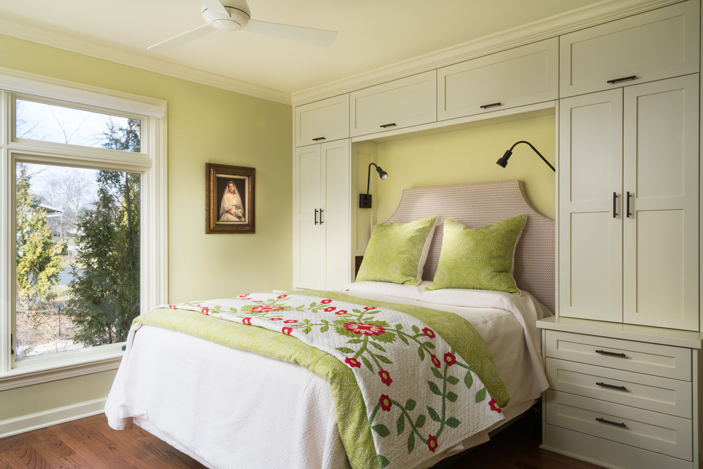 Imagen de dormitorio principal tradicional renovado de tamaño medio sin chimenea con paredes amarillas, suelo de madera en tonos medios y suelo marrón