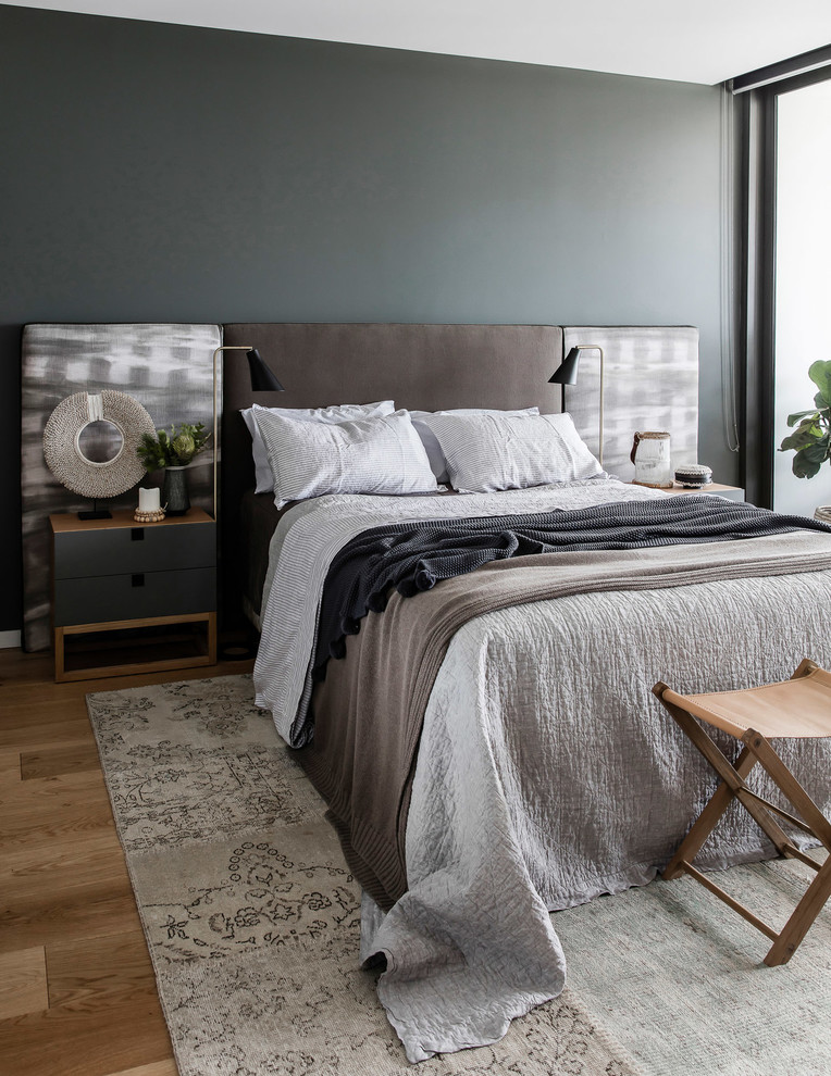 Diseño de dormitorio principal costero con paredes grises, suelo de madera en tonos medios y suelo marrón