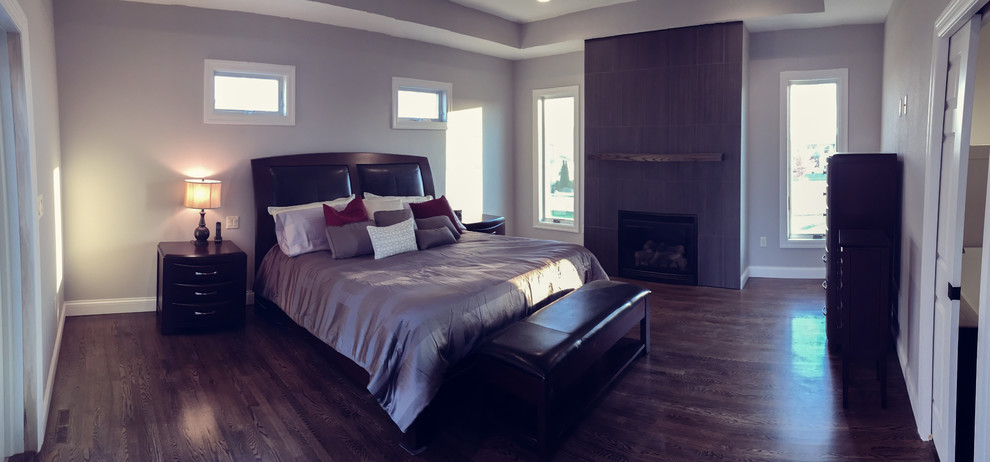 Cette image montre une grande chambre parentale design avec parquet foncé, un manteau de cheminée en carrelage, un mur beige et une cheminée standard.