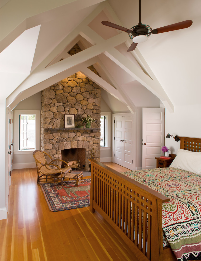 Inspiration pour une chambre parentale marine avec un mur blanc, un sol en bois brun, une cheminée standard et un manteau de cheminée en pierre.