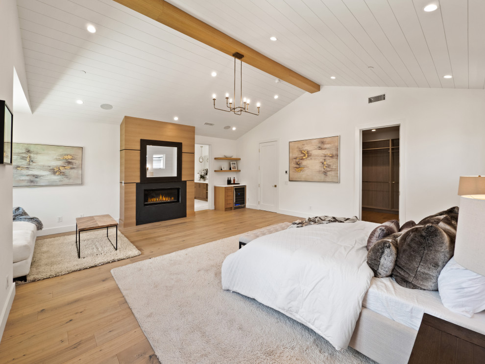 Cette photo montre une très grande chambre parentale nature avec un mur blanc, parquet clair, une cheminée standard, un manteau de cheminée en plâtre, un plafond voûté et du lambris.