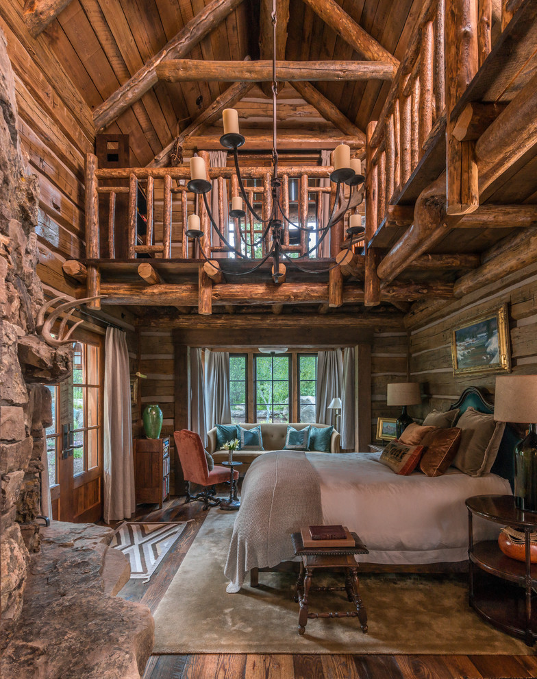 Cette photo montre une chambre parentale montagne avec un sol en bois brun, une cheminée standard et un manteau de cheminée en pierre.