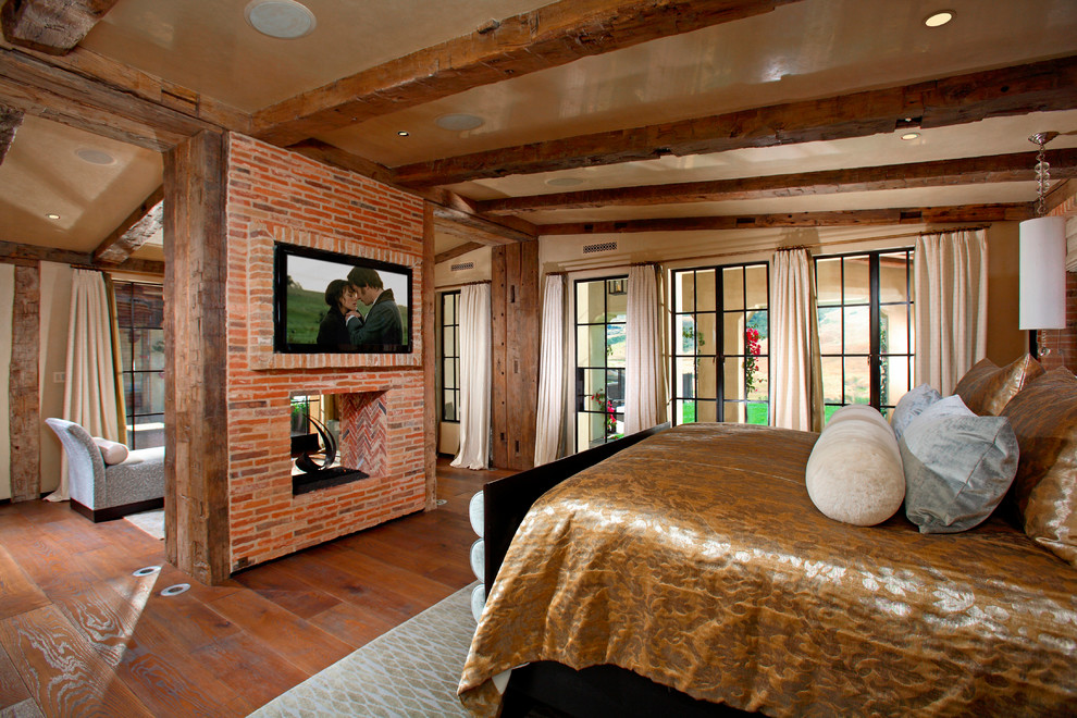 Example of a tuscan master dark wood floor bedroom design in Orange County with beige walls, a two-sided fireplace and a brick fireplace