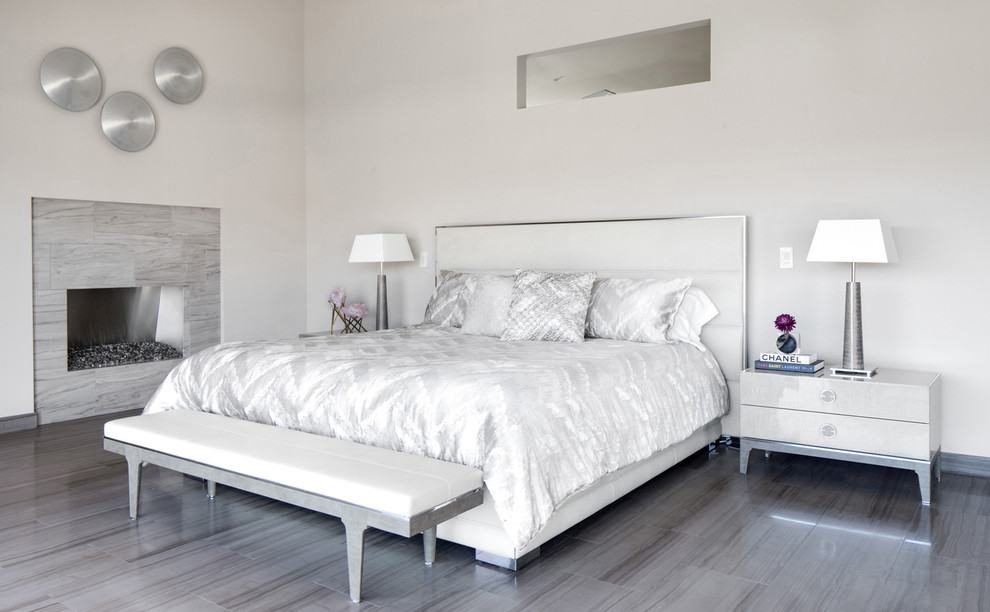 Свежая идея для дизайна: большая хозяйская спальня в современном стиле с белыми стенами, полом из керамической плитки, стандартным камином, фасадом камина из плитки и серым полом - отличное фото интерьера