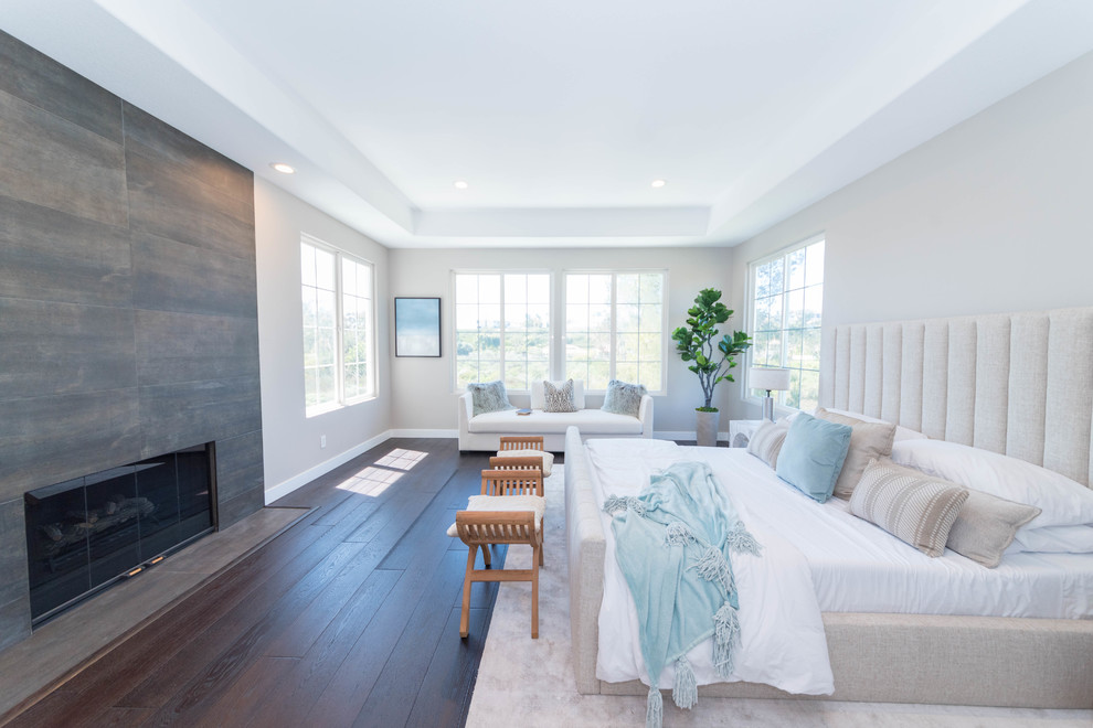Cette image montre une grande chambre parentale design avec un mur gris, parquet foncé, une cheminée standard, un manteau de cheminée en bois et un sol marron.