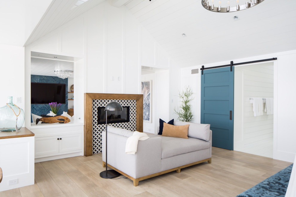 Geräumiges Maritimes Hauptschlafzimmer mit weißer Wandfarbe, hellem Holzboden, Kamin, gefliester Kaminumrandung und beigem Boden in Orange County