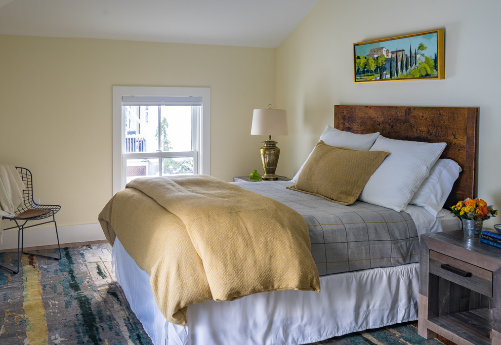 Modelo de dormitorio clásico renovado con paredes amarillas, suelo de madera en tonos medios y suelo marrón