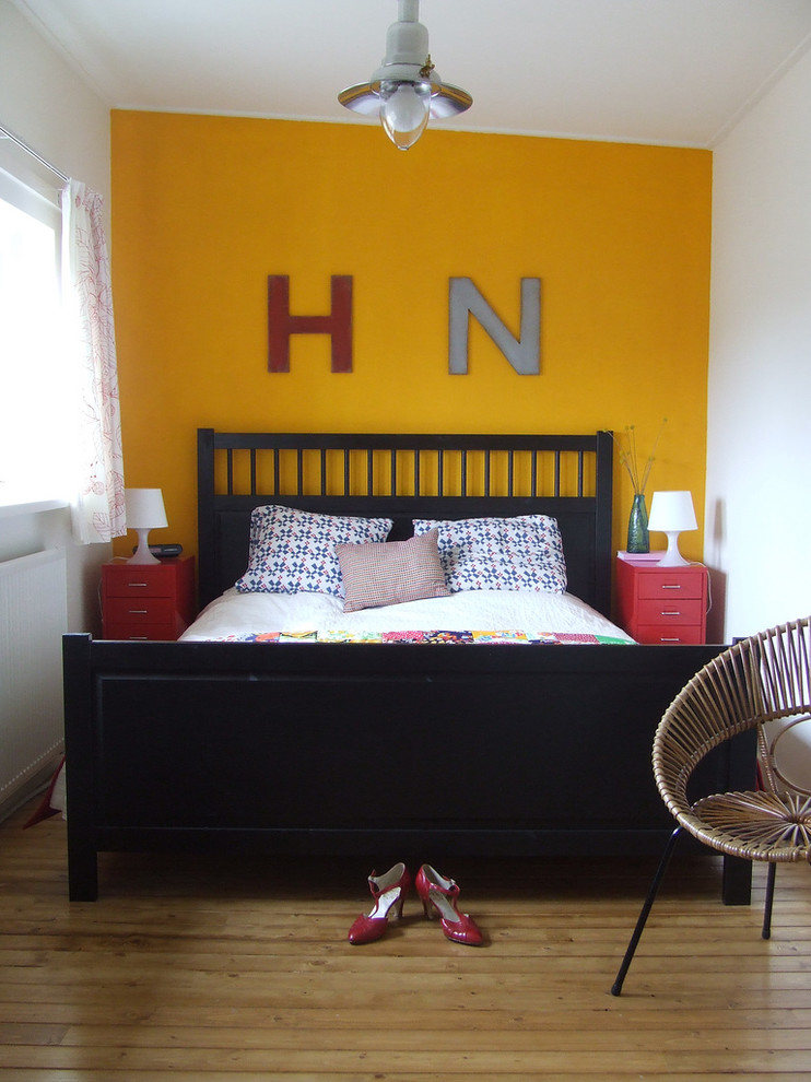 Diseño de dormitorio ecléctico sin chimenea con paredes amarillas y suelo de madera en tonos medios