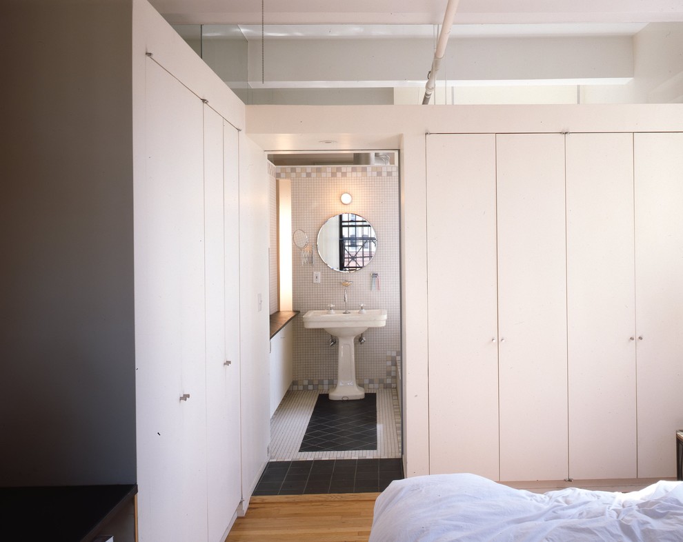 Ejemplo de dormitorio tipo loft urbano con paredes blancas y suelo de madera en tonos medios
