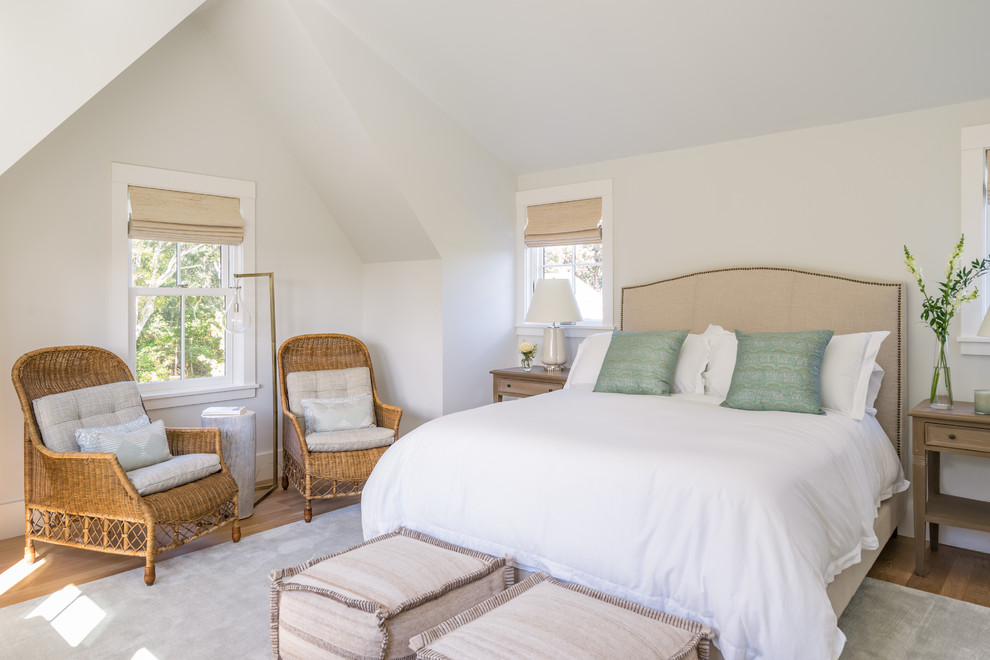 Diseño de dormitorio principal costero grande sin chimenea con paredes blancas, suelo de madera en tonos medios y suelo marrón