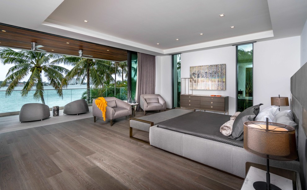 This is an example of an expansive contemporary master, grey and brown and grey and silver bedroom in Miami with white walls, medium hardwood flooring, grey floors and no fireplace.
