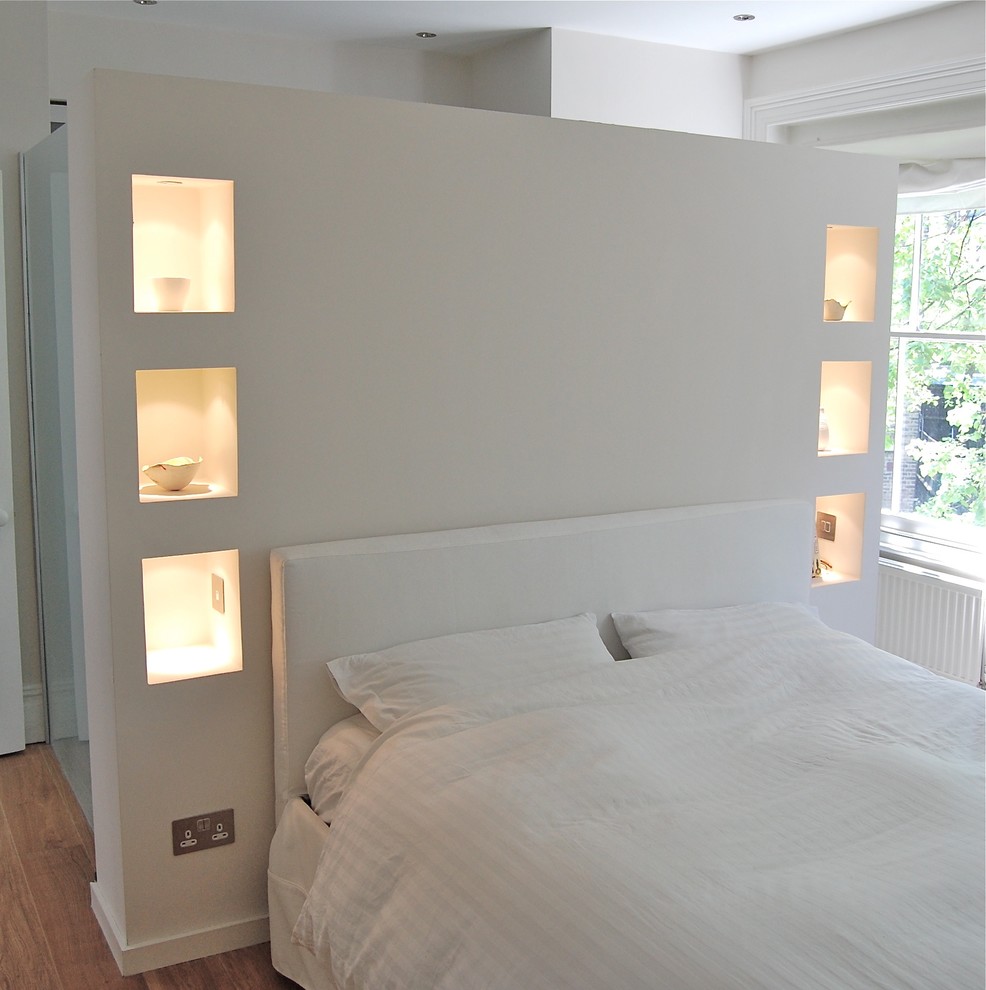 Cette image montre une chambre parentale design de taille moyenne avec un mur blanc et un sol en bois brun.