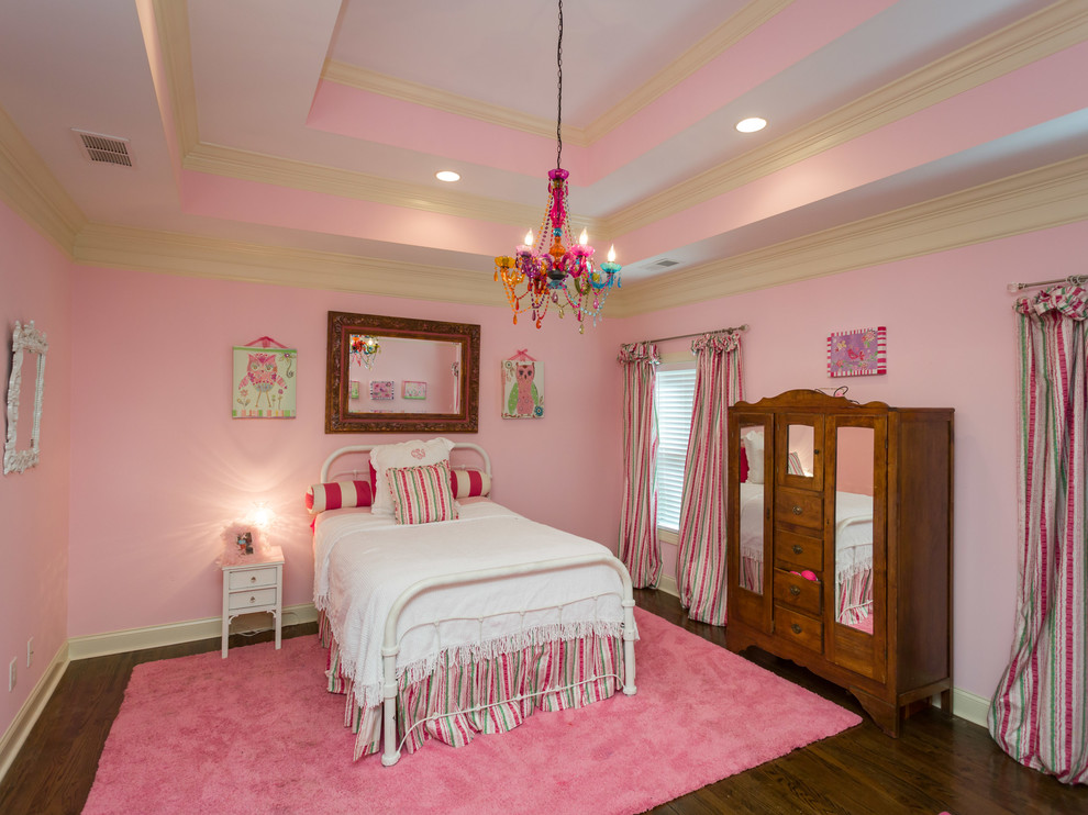 Modelo de habitación de invitados de estilo americano grande sin chimenea con paredes rosas y suelo de madera en tonos medios