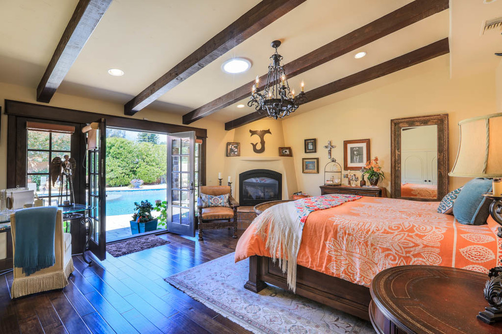 Inspiration for a large mediterranean master bedroom in Los Angeles with beige walls, dark hardwood flooring, a corner fireplace, a plastered fireplace surround and brown floors.
