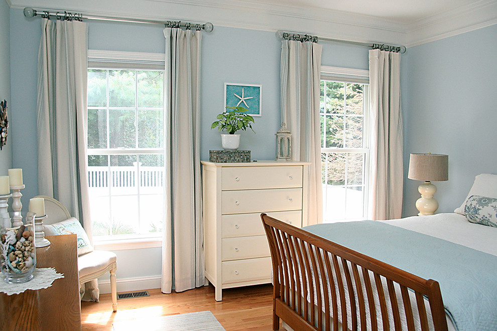 Diseño de dormitorio principal costero grande sin chimenea con paredes azules, suelo de madera en tonos medios y suelo marrón