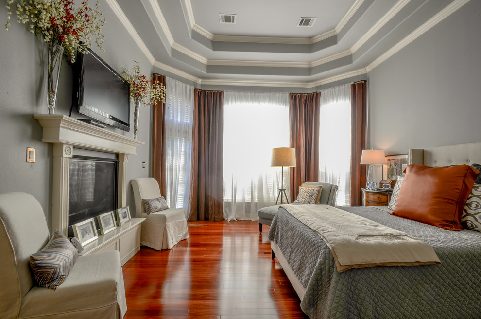 オースティンにあるトランジショナルスタイルのおしゃれな主寝室 (グレーの壁、無垢フローリング、標準型暖炉、オレンジの床) のインテリア