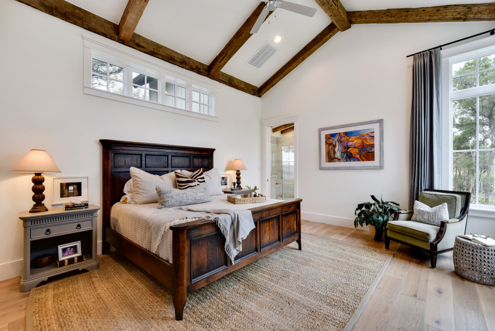 Modelo de dormitorio principal de estilo de casa de campo grande con paredes blancas, suelo de madera clara y suelo beige