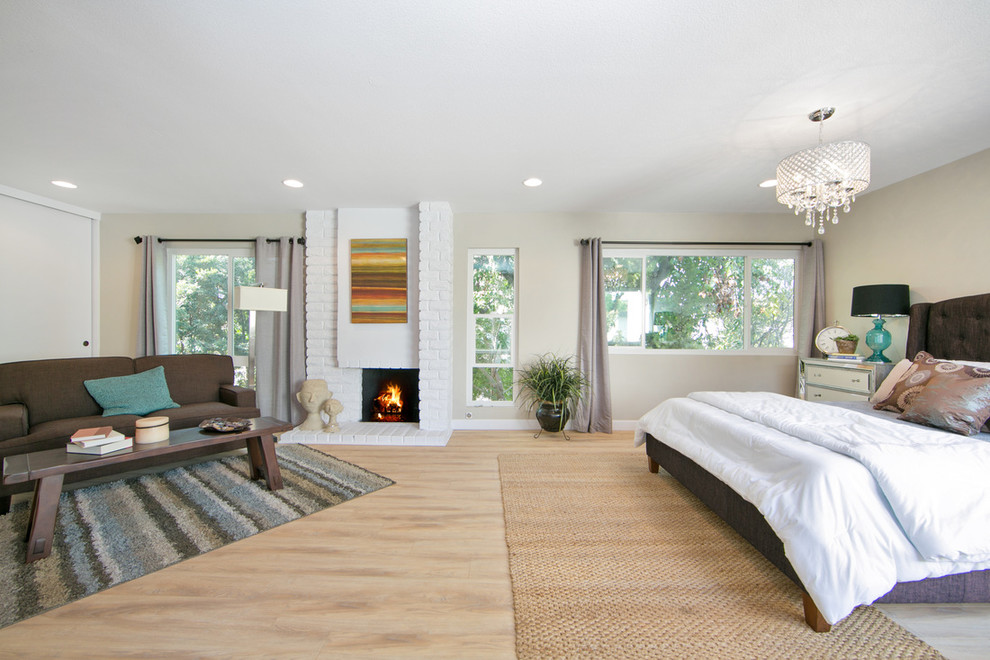 Design ideas for a large contemporary master bedroom in Orange County with beige walls, light hardwood flooring, a standard fireplace, a brick fireplace surround and brown floors.