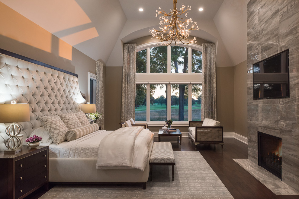 This is an example of an expansive contemporary master bedroom in Detroit with beige walls, dark hardwood flooring, a two-sided fireplace, a tiled fireplace surround and brown floors.