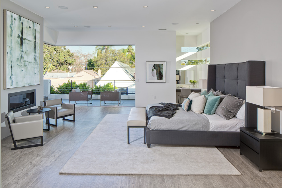 Large contemporary master bedroom in Los Angeles with a ribbon fireplace, white walls, light hardwood flooring and a plastered fireplace surround.