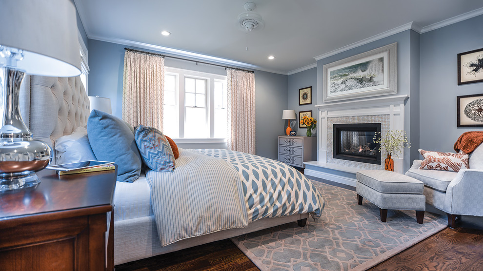Foto de dormitorio principal con paredes azules, suelo de madera en tonos medios, todas las chimeneas, marco de chimenea de baldosas y/o azulejos y suelo marrón